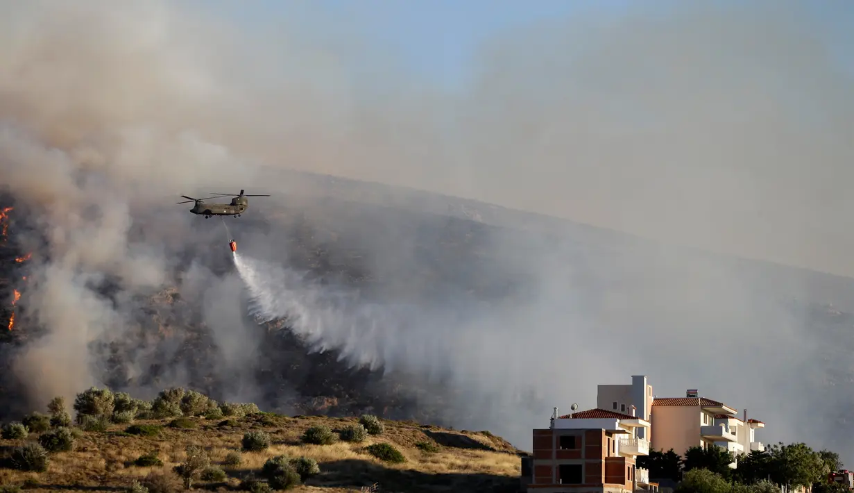Helikopter menjatuhkan air untuk memadamkan kebakaran lahan api di daerah Kalyvia, dekat Athena, Senin (31/7). Sebanyak 5 unit helikopter dikerahkan dalam operasi pengeboman air di sejumlah titik api. (AP/Thanassis Stavrakis)