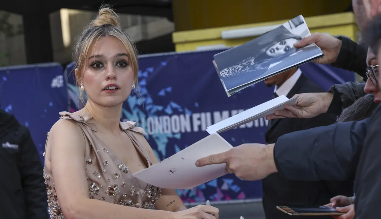 Aimee Lou Wood memberikan tanda tangan kepada penggemar saat menghadiri pemutaran perdana film 'Living' selama Festival Film London 2022 di London, Minggu, 9 Oktober 2022. Aimee memilih palet riasan perunggu yang menonjolkan fitur alaminya dengan sapuan lipstik nude. (Photo by Vianney Le Caer/Invision/AP)