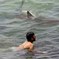 Seekor hiu berenang melewati perenang di Laut Mediterania di lepas pantai kota Hadera di utara Tel Aviv, Israel, Selasa (20/4/2021). Fenomena yang menjadi perhatian warga ini diduga akibat suhu air laut Mediterania berubah menjadi hangat. (JACK GUEZ/AFP)