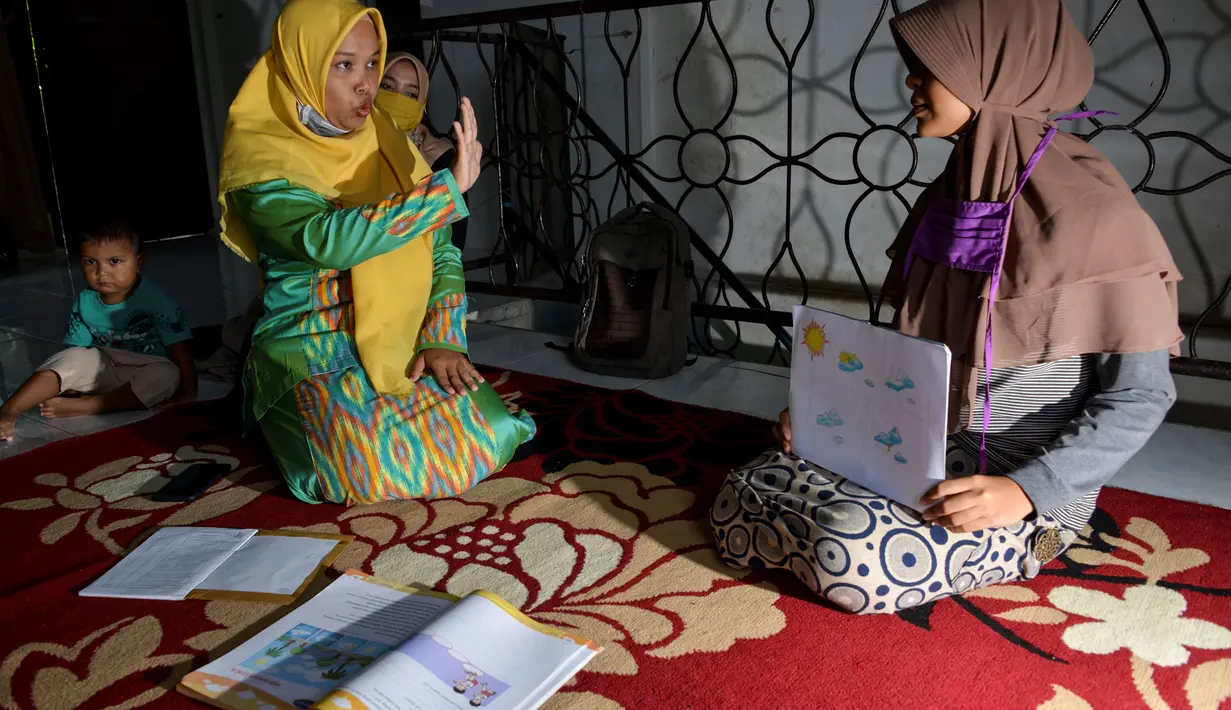 Seorang guru (kedua kiri) menggunakan bahasa isyarat membimbing siswa tunarungu di rumahnya di Pekan Bada, dekat Banda Aceh (14/9/2020). Para guru telah membimbing siswa yang kekurangan akses ke internet untuk kelas online di rumah mereka setelah wabah virus merebak. (AFP Photo/Chaideer Mahyuddin)