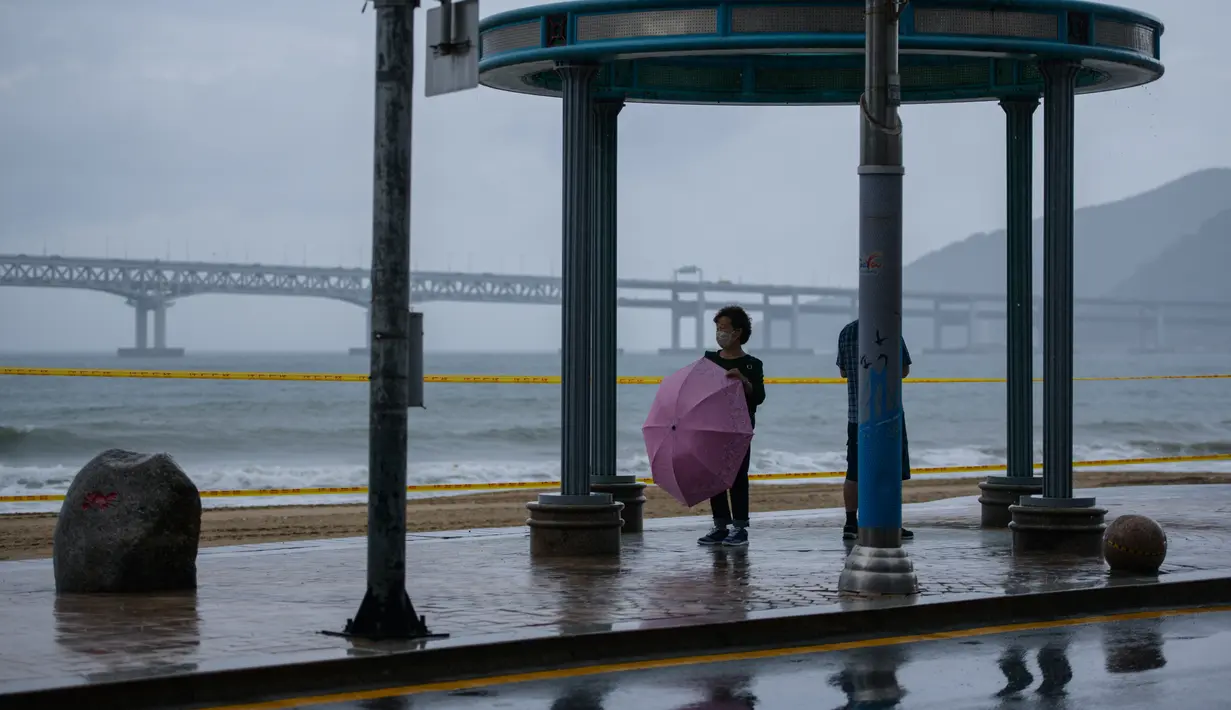 Seorang wanita berdiri dengan umbrealla di depan pantai Gwangalli di Busan (2/9/2020). Penerbangan dihentikan di Korea Selatan dan peringatan badai dikeluarkan di kedua sisi semenanjung Korea sebagai topan yang diperkirakan akan menjadi salah satu yang terkuat. (AFP/Ed Jones)