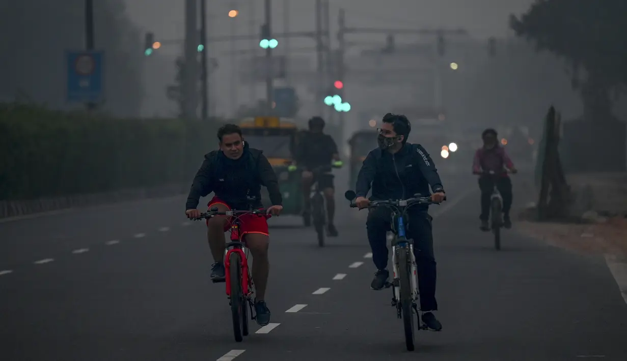 Pesepeda melintas di sepanjang jalan di tengah kondisi kabut asap yang menyelimuti New Delhi, India, Minggu (7/11/2021). Ibu kota New Delhi diselimuti udara beracun pada Sabtu kemarin karena tingkat polusi yang sangat tinggi pasca-perayaan festival besar agama Hindu. (Money SHARMA/AFP)