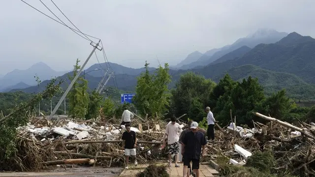 Warga setempat melintasi jalan yang rusak dan dipenuhi ranting-ranting pohon yang patah setelah hujan deras mengguyur kota kecil Taishitun, Distrik Miyun, di pinggiran Beijing, China, Senin, (28/7/2025).