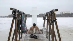 Seorang pria mandi di air dingin sungai Klyazma selama perayaan Epiphany tradisional saat suhu turun hingga sekitar -20 derajat di luar Moskow, Rusia (19/1/2021). berendam di kolam air es diyakini memiliki kekuatan khusus untuk melindungi dan menyembuhkan. (AP Photo/Alexander Zemlianichenko Jr)