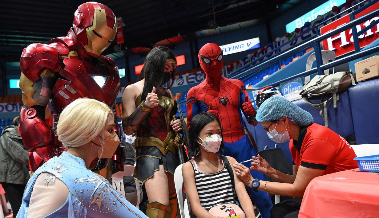 Dua orang berkostum superhero berpose dengan seorang anak yang menerima vaksin Covid-19 Pfizer-BioNtech untuk anak-anak berusia 5-11 di sebuah gym di San Juan City, pinggiran kota Manila, Filipina pada 7 Februari 2022. (Ted ALJIBE / AFP)