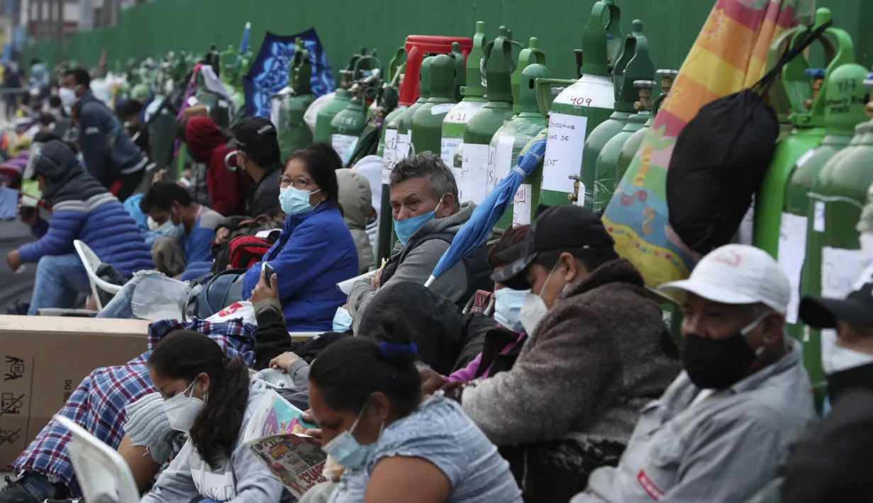 Orang-orang duduk di dekat tabung oksigen kosong mereka saat menunggu toko isi ulang dibuka di lingkungan San Juan de Lurigancho di Lima, Peru, Senin (22/2/2021). Menurut pemerintah, permintaan oksigen medis tumbuh 200 persen di Peru di tengah gelombang kedua Covid-19. (AP Photo/Martin Mejia)