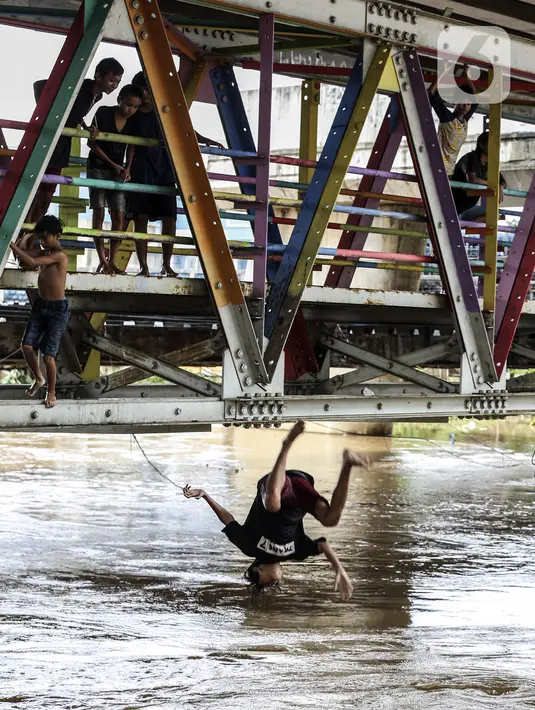 Seorang anak melompat ke Sungai Ciliwung saat banjir melanda Jalan Bina Warga Rt 005/Rw 07 Kelurahan Rawa Jati, Jakarta, Senin (8/2/2021). Banjir setinggi 60-190 cm tersebut disebabkan oleh luapan air Sungai Ciliwung dan curah hujan Jakarta yang tinggi. (Liputan6.com/Johan Tallo)