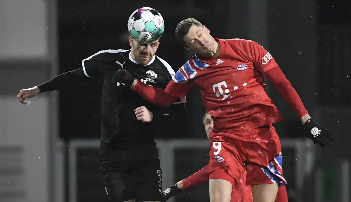 Striker Bayern Munich, Robert Lewandowski (kanan) berduel udara dengan bek tim Divisi 2 Holstein Kiel, Marco Komenda dalam laga babak kedua Piala DFB Pokal 2020/21 di Kiel, Rabu (13/1/2021). Bayern Munich kalah dari Holstein Kiel lewat adu penalti 5-6 (2-2). (AFP/Fabian Bimmer/Pool)