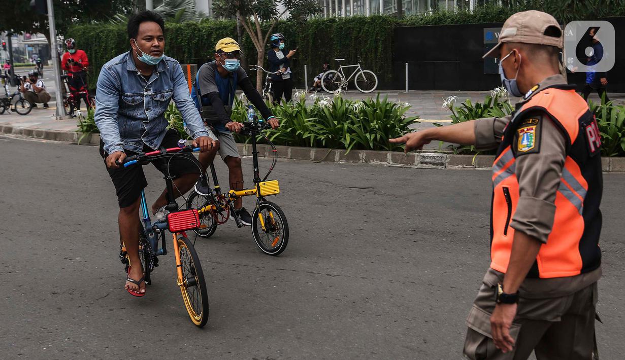 Satpol PP menghentikan pesepeda yang tidak mengenakan masker dengan benar di kawasan Bundaran HI, Jakarta, Minggu (17/1/2021). Pemerintah terus melakukan berbagai upaya guna mencegah penyebaran COVID-19 dan menurunkan angka masyarakat yang terpapar virus corona. (Liputan6.com/Johan Tallo)