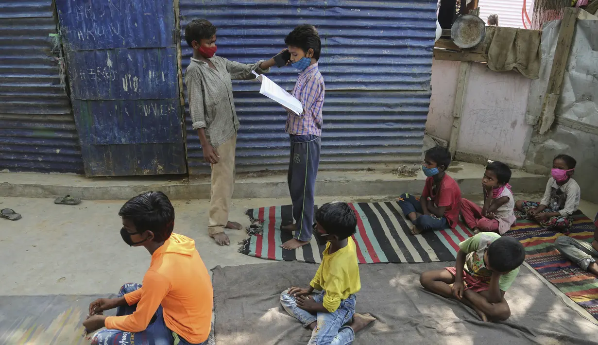 Seorang siswa memegang ponsel untuk yang lain sehingga dia dapat mendengarkan instruksi dari seorang guru saat menghadiri kelas online di sebuah perkampungan kumuh di pinggiran Jammu, India, Senin, 14 Juni 2021.  (AP Photo/Channi Anand)