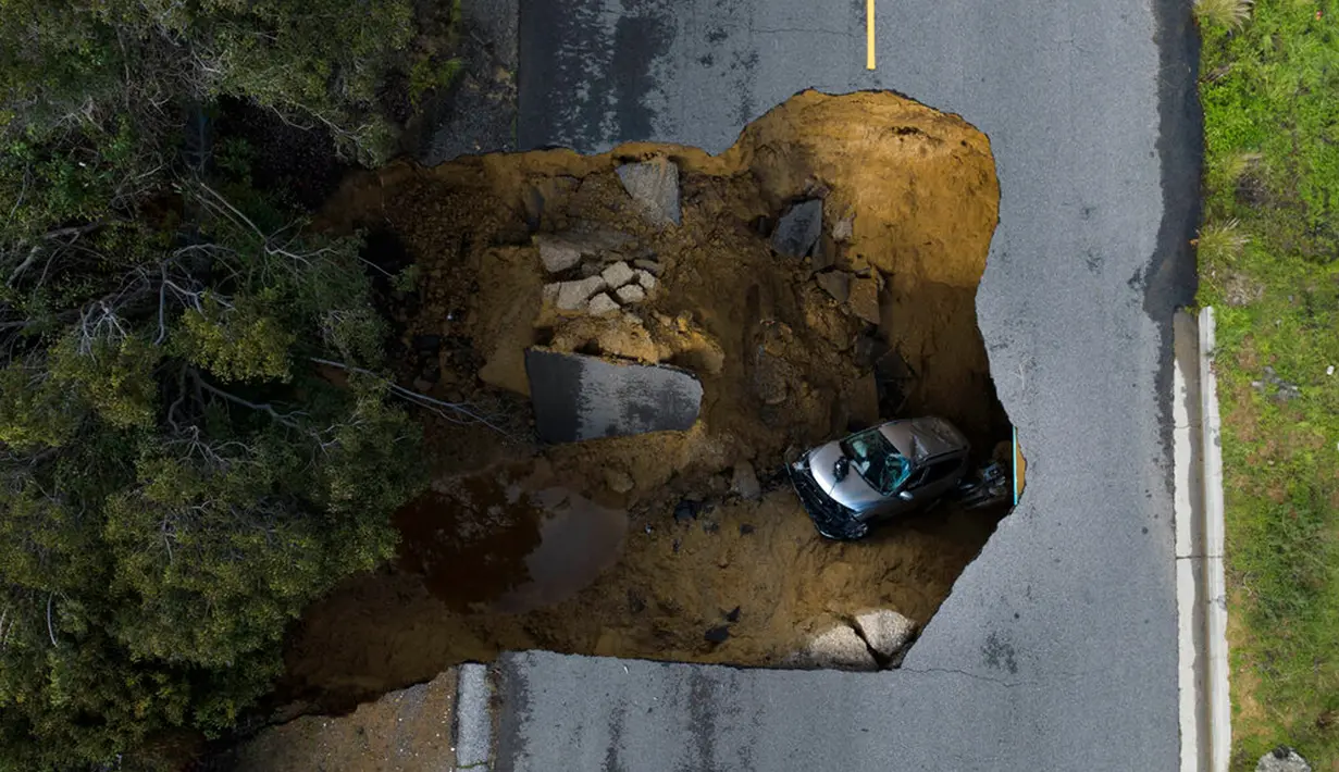 Foto drone memperlihatkan sebuah kendaraan terjebak dalam lubang runtuhan di Chatsworth, Los Angeles, California, Amerika Serikat, 10 Januari 2023. Serangkaian badai yang menghantam California telah menyebabkan jalanan terendam banjir, gelombang tinggi air laut, sungai meluap, dan memaksa ribuan orang untuk mengungsi. (AP Photo/Jae C. Hong)