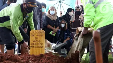 Istri mantan penggawa Timnas Indonesia Ricky Yacobi, Harly Ramayani (duduk tengah) menyaksikan proses pemakaman suaminya di TPU Tanah Kusir, Jakarta, Sabtu (21/11/2020). Ricky Yacobi meninggal dunia pada Sabtu (21/11) akibat serangan jantung pada usia 57 tahun. (Liputan6.com/Helmi Fithriansyah)