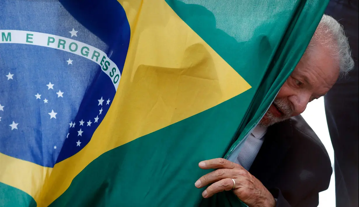 Mantan presiden Brasil (2003-2010) dan kandidat presiden dari Partai Pekerja (PT) berhaluan kiri, Luiz Inacio Lula da Silva, muncul di belakang bendera nasional Brasil selama kampanye di Sao Mateus, Negara Bagian Sao Paulo, Brasil, Senin (17/10/2022). Lula da Silva dan presiden Jair Bolsonaro akan menghadapi putaran kedua pemilihan presiden pada 30 Oktober, dengan ekspektasi persaingan ketat mendorong kedua belah pihak untuk mengintensifkan kampanye pemilihan. (Miguel SCHINCARIOL / AFP)