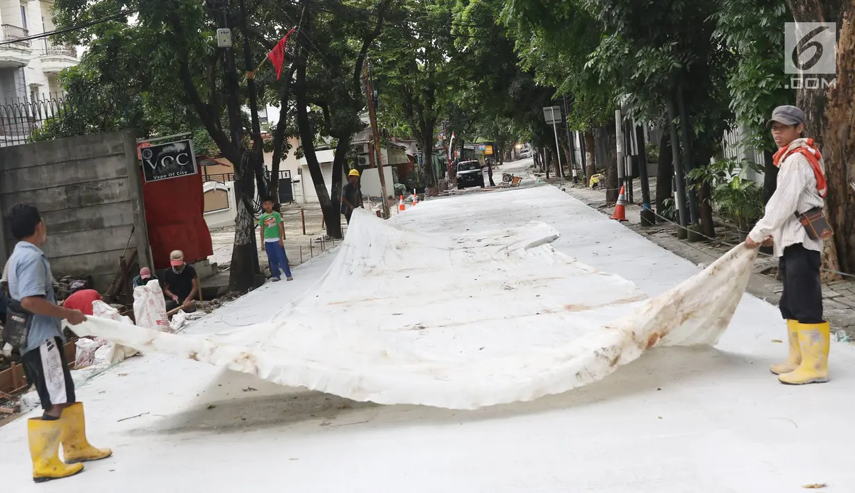 Pekerja menutupi beton yang sudah di cor dengan kain di Jalan Pejaten Raya di Jakarta Selatan (22/11). Proyek pembetonan dan peninggian badan jalan ini ditargetkan rampung pada akhir November. (Liputan6.com/Immanuel Antonius)