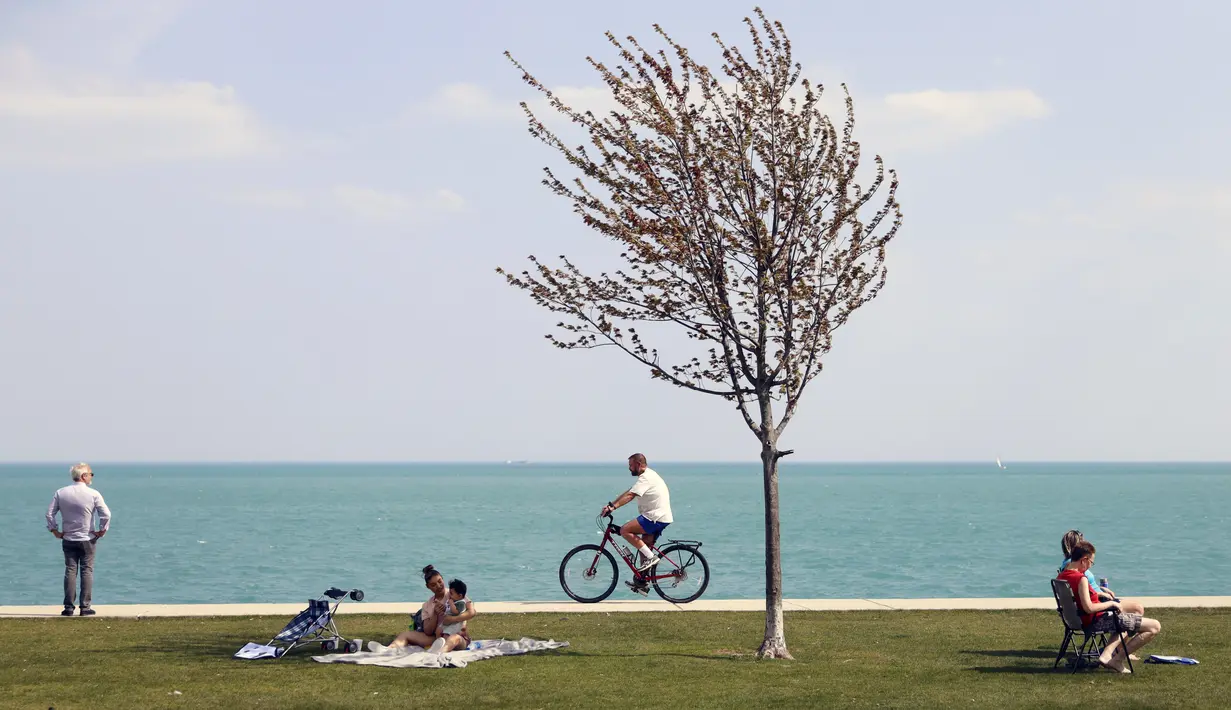 Orang-orang memanfaatkan cuaca musim semi yang hangat di sepanjang Danau Michigan, Chicago, Selasa (27/4/2021). Warga AS yang telah menerima vaksin COVID-19 tidak lagi diwajibkan mengenakan masker saat berada di luar ruangan kecuali berada di tengah kerumuman orang asing. (AP Photo/Shafkat Anowar)