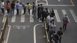 Warga dan pekerja kantor yang mengenakan masker berbaris di jalan untuk pengujian virus corona massal di dekat kompleks perumahan dan perkantoran komersial di kawasan pusat bisnis, Beijing, Senin (25/4/2022). (AP Photo/Andy Wong)