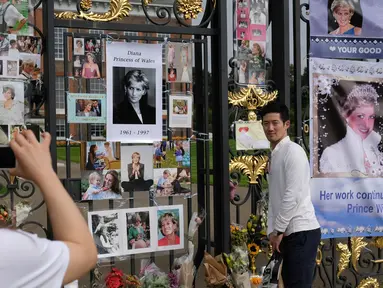 Seorang turis mengambil foto temannya yang berpose dekat memorabilia Putri Diana di luar Istana Kensington, London, Selasa (29/8). Bunga, foto hingga lilin diletakkan di luar Istana untuk mengenang 20 tahun kematian Putri Diana. (AP Photo/Alastair Grant)