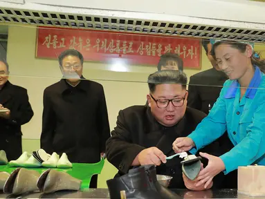 Pemimpin Korea Utara, Kim Jong-Un dibantu pekerja mengelem sepatu saat mengunjungi pabrik sepatu Wonsan, Korea Utara (3/12). (Photo by KCNA VIA KNS / various sources / AFP)