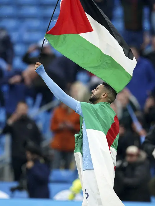 Gelandang Manchester City, Riyad Mahrez mengibarkan bendera Palestina saat merayakan timnya meraih gelar Liga Inggris di stadion Etihad, Minggu (23/5/2021). Pemain Aljazair ini melakukan hal tersebut bentuk dukungan kepada Palestina di tengah konflik dengan Israel. (AP Photo/Dave Thompson, Pool)