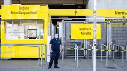 Petugas keamanan mengenakan masker berjaga-jaga di luar pusat pengujian COVID-19 di stadion milik Borussia Dortmund di Jerman (4/4/2020). Kamar-kamar di tribun utara Stadion Westfalen dipersiapkan untuk menampung orang-orang yang diduga terinfeksi COVID-19. (Xinhua/Joachim Bywaletz)