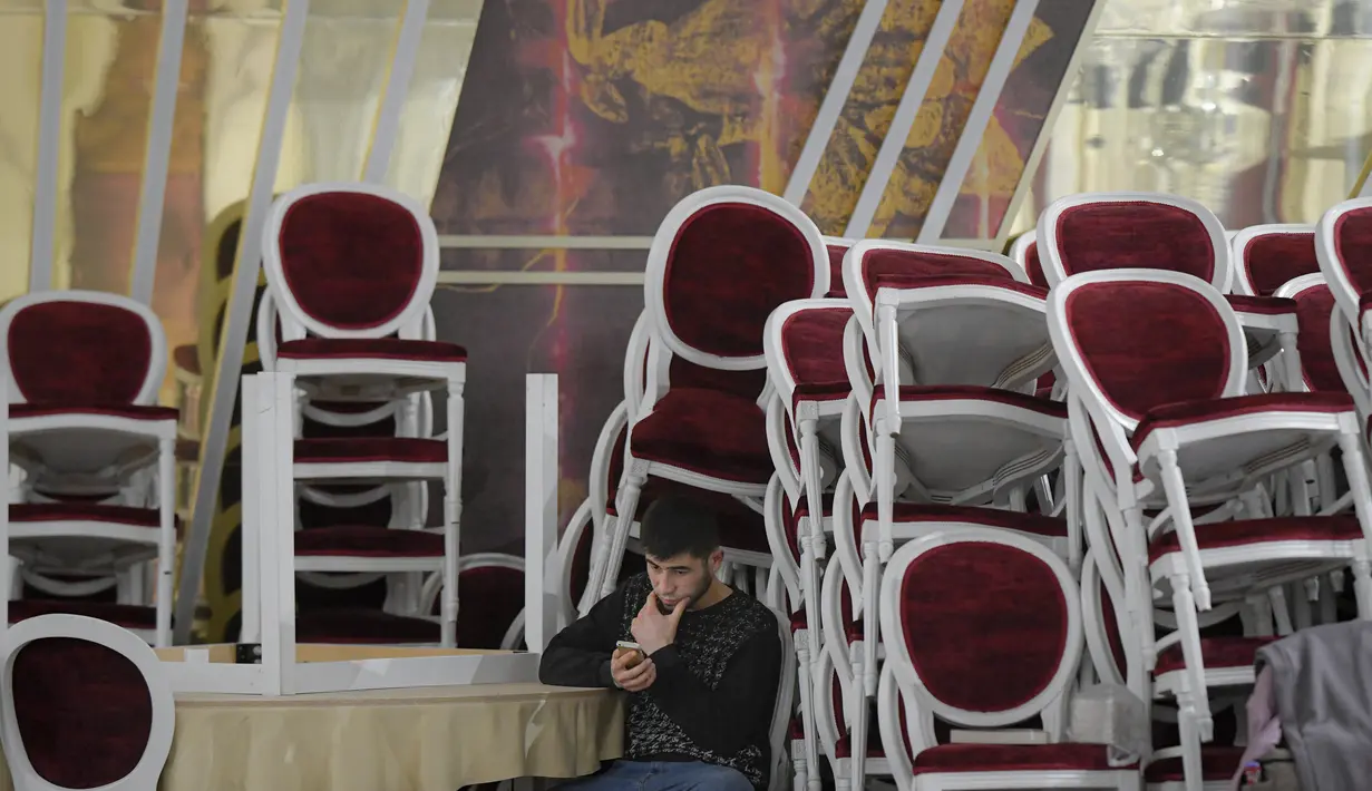 Seorang pria duduk dekat tumpukan kursi yang dipindahkan untuk menampung pengungsi yang melarikan diri dari invasi Rusia terhadap Ukraina, di dalam ballroom yang menjadi tempat penampungan pengungsi darurat di hotel & spa bintang 4, di Suceava, Rumania, 4 Maret 2022. (AP Photo/Andreea Alexandru)