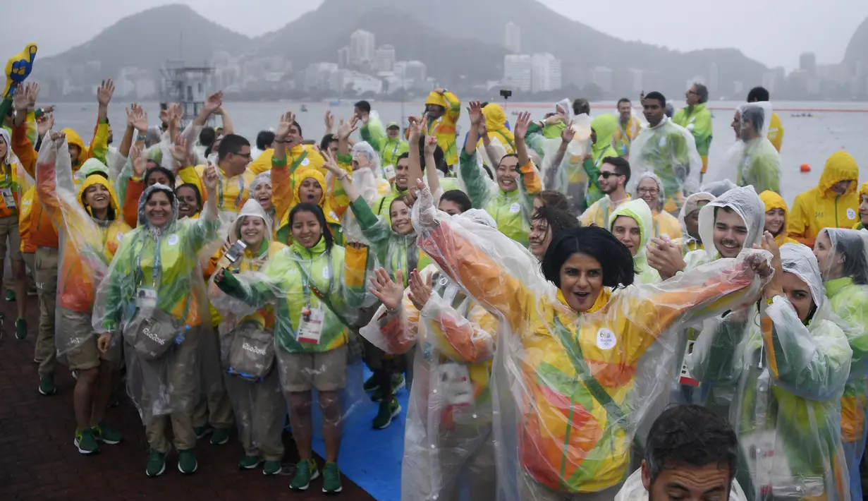 Sejumlah relawan bersorak sambil mengenakan jas hujan usai dibatalkannya kompetisi cabang dayung Olimpiade 2016 akibat cuaca buruk di stadion Lagoa, Rio de Janeiro, 10 Agustus 2016. (AFP PHOTO/Damien Meyer)