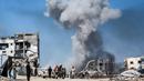 Orang-orang bergerak melewati bangunan yang hancur berlatar belakang kepulan asap menyusul serangan Israel di Jabalia, Jalur Gaza utara pada 25 Mei 2025. (Bashar TALEB/AFP)