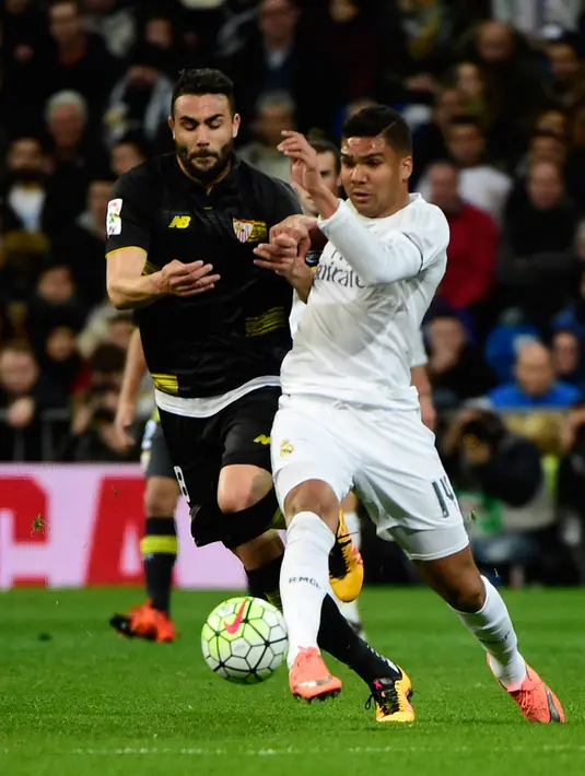 Gelandang Real Madrid, Casemiro (kanan) berebut bola dengan gelandang Sevilla, Iborra pada Liga Spanyol di Stadion Santiago Bernabeu (21/3). Real Madrid menang besar atas Sevilla dengan skor 4-0. (AFP/PIERRE-PHILIPPE Marcou)