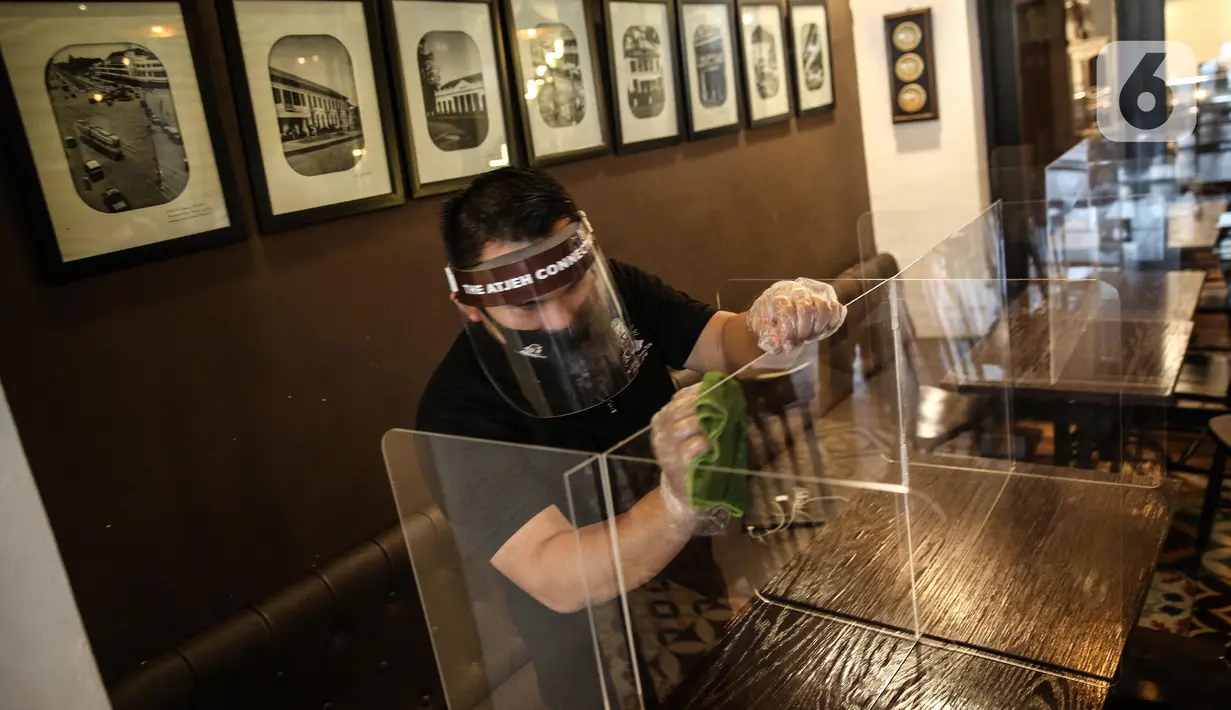 Pekerja membersihkan papan pelindung akrilik usai digunakan pengunjung di The Atjeh Connection Coffee and Resto, Jakarta, Senin (8/6/2020). Tempat ini siap menerapkan protokol kesehatan dalam menerapkan tatanan kehidupan baru atau ‘new normal’. (Liputan6.com/Faizal Fanani)