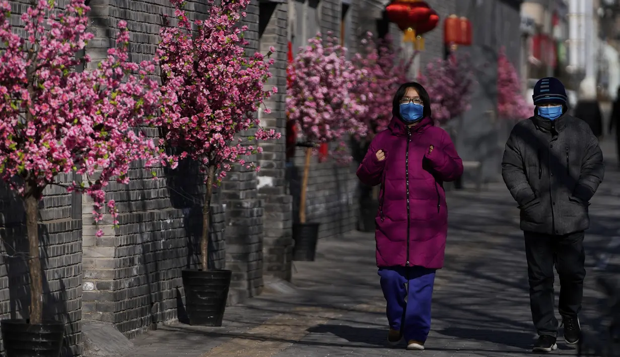 Warga mengenakan masker untuk membantu melindungi dari virus corona berjalan melewati dekorasi bunga dan lentera untuk Tahun Baru Imlek mendatang di Beijing, Kamis (27/1/2022). (AP Photo/Andy Wong)