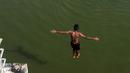 Seorang pemuda India melompat ke dalam sungai yang tercemar di pinggiran Chennai, India, Rabu (5/4). Sejumlah warga di India biasa mandi di sungai saat cuaca panas. (AFP PHOTO / ARUN SANKAR)