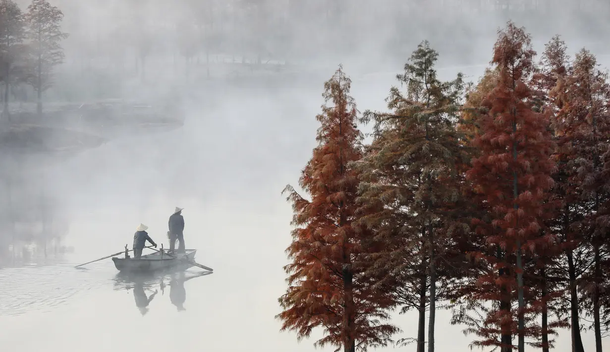 Warga mengendarai perahu di Danau Tianquan yang berselimut kabut di Xuyi di Provinsi Jiangsu, China (20/11/2019). Memasuki musik dingin, pemandangan Danau Tianquan berselimut kabut tipis berpadu dengan pepohonan berdaun kemerahan terlihat lebih indah dari biasanya. (AFP Photo/Str)