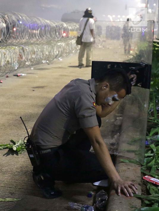 Personil Kepolisian menahan mual akibat gas air mata saat menghalau massa yang berlaku anarkis di sekitar depan Gedung Bawaslu, Jalan MH Thamrin, Jakarta, Rabu (22/5/2019). Aksi unjuk rasa yang dimotori GNKR berakhir ricuh. (Liputan6.com/HelmiFithriansyah)
