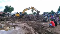 Warga menyaksikan ekskavator membersihkan puing pada daerah yang terkena banjir bandang di Waiwerang, Pulau Adonara, Nusa Tenggara Timur, Selasa (6/4/2021). Tim penyelamat terus menggali puing tanah longsor untuk mencari korban yang terkubur usai bencana banjir bandang. (AP Photo/Rofinus Monteiro)