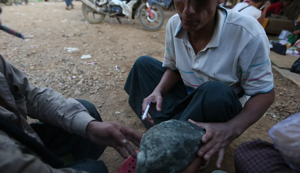 Seorang penambang melihat batu giok dengan jarum suntik berisikan heroin menempel ditubuhnya di Tambang batu giok di Hpakant, Myanmar, 29 November 2015. Kecanduan narkotika sudah merabak pada penambang batu giok. (REUTERS/Soe Zeya Tun)