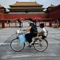 Seorang perempuan mengendarai sepedanya dengan seorang anak duduk di kursi belakang melewati Kota Terlarang di Beijing, China, Selasa (7/6/2022). Pemerintah melonggarkan beberapa pembatasan Covid-19 dengan sebagian besar museum gedung bioskop, dan pusat kebugaran diizinkan beroperasi hingga 75 persen dari kapasitas. (WANG Zhao / AFP)