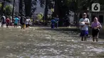 Warga melintasi genangan air yang merendam jalan di kawasan Kampung Makasar, Jakarta Timur, Senin (7/7/2025). (Liputan6.com/Herman Zakharia)