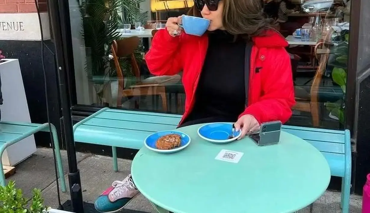 Menikmati kopi santai di cafe, Reza tampil dengan layering outfit memadukan puffer jacket merah dengan inner hitam. [Foto: IG/rezaartameviaofficial].