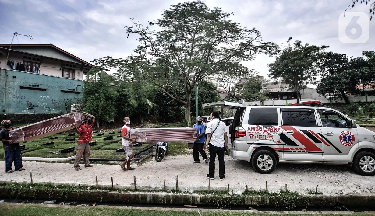 Pekerja membawa peti jenazah yang selesai dibuat untuk dipindahkan ke ambulans di TPU Pondok Kelapa, Jakarta, Selasa (13/7/2021). Berbanding terbalik pada masa sebelum Lebaran, dalam sehari pekerja hanya memproduksi 10-15 peti jenazah. (merdeka.com/Iqbal S Nugroho)