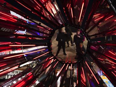 Orang-orang memotret "Out of The Dark" karya Tom Lambert, sebagai bagian dari festival Winter Lights di Canary Wharf, London, Rabu (18/1/2023). Festival Winter Lights kembali ke Canary Wharf untuk pertama kalinya sejak 2020. (AP Photo/Alberto Pezzali)