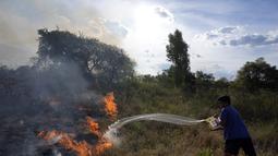 Seorang warga mencoba menyiram padang rumput yang terbakar selama kebakaran semak di lingkungan Banco San Miguel di Asuncion, Paraguay (18/1/2022). Cuaca kering yang tidak biasa memicu kebakaran di ladang terbuka, peternakan pribadi, dan lahan publik di sekitar kota. (AP Photo/Jorge Saenz)