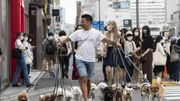 Petualang anjing profesional Nobuaki Moribe memimpin hewan peliharaan kliennya melintasi persimpangan di Tokyo (28/5/2021). Jepang memperpanjang keadaan darurat virus corona di Tokyo dan daerah lain selama 20 hari lagi pada hari Jumat. (AP Photo/Hiro Komae)