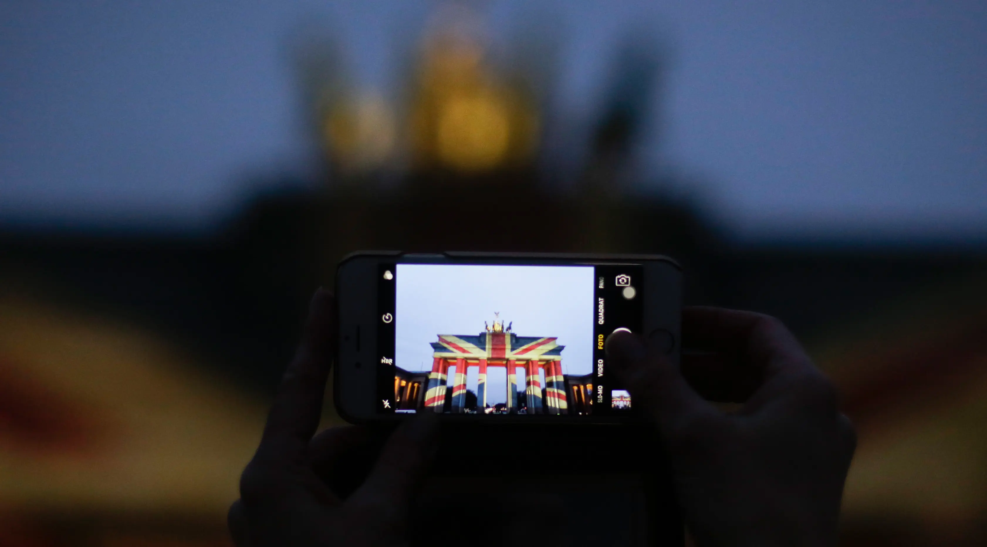 Seorang pengunjung mengambil gambar dari gerbang Brandenburg yang diterangi dengan warna bendera kebangsaan Inggris sebagai bentuk turut berduka cita atas teror London, di ibu kota Jerman, Berlin, Kamis (23/3). (AP Photo/Markus Schreiber)