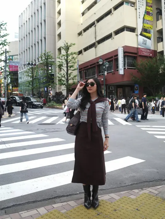 Saat berada di area persimpangan Tokyo, Febby tampil dengan nuansa preppy modern. Ia mengenakan striped top yang dipadukan midi skirt cokelat high waist. Sweater cokelat yang disampirkan di bahu memberi sentuhan old money aesthetic yang kini kembali tren. [@febbyrastanty].