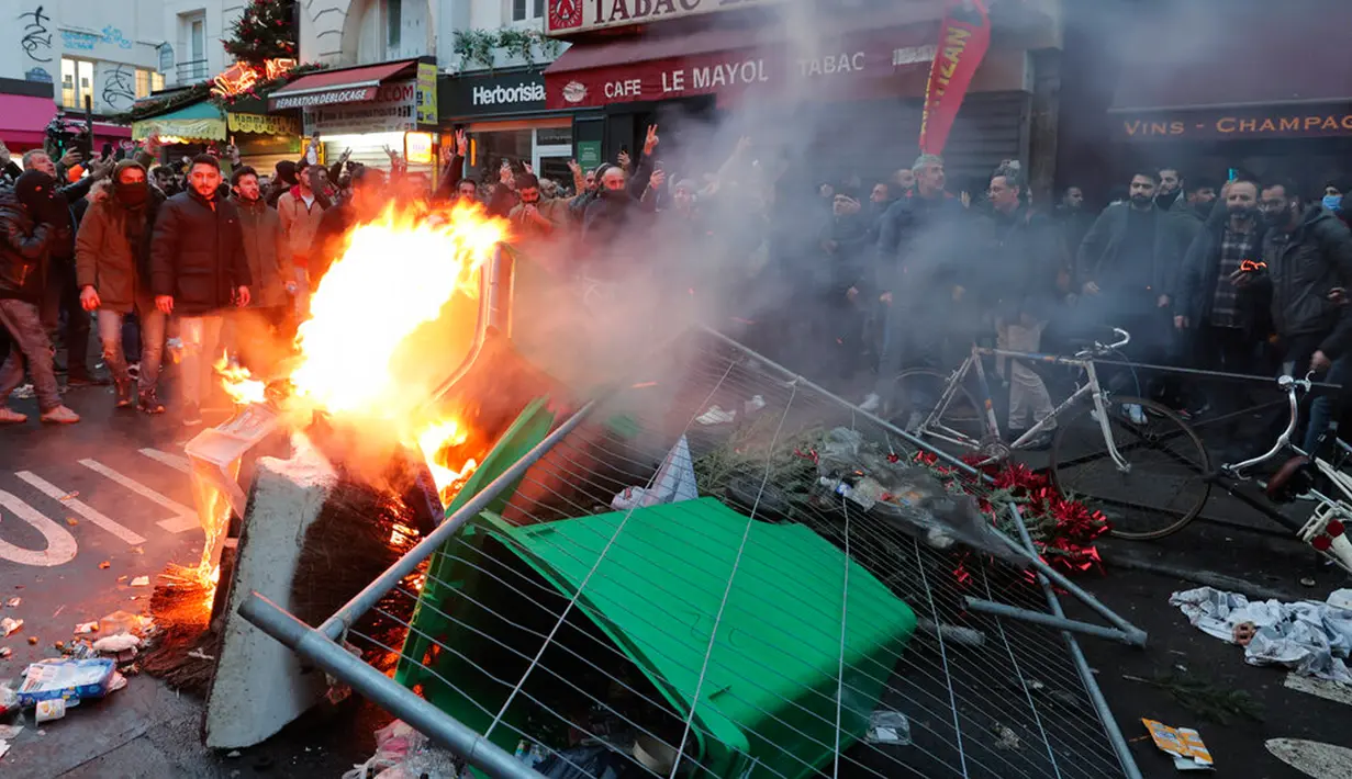 Anggota komunitas Kurdi berdiri dekat barikade yang terbakar saat bentrok dengan petugas polisi di TKP tempat terjadinya penembakan di Paris, Prancis, 23 Desember 2022. Aksi demo itu berlangsung di sekitar Kurdish Center dan dihadiri ratusan orang Kurdi untuk memprotes penembakan yang diduga bermotif rasisme. (AP Photo/Lewis Joly)