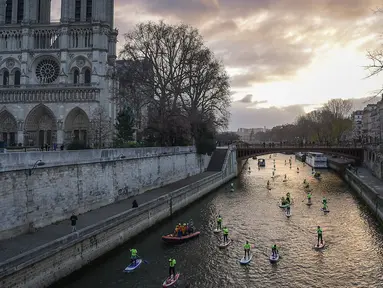 Para peserta mengambil bagian dalam Nautic Paddle Race dekat katedral Notre-Dame di Paris, Minggu (9/12). Sekitar 800 orang mengikuti lomba dayung sambil berdiri terbesar di dunia sejauh 11 km menyeberangi sungai Seine. (Lucas BARIOULET/AFP)