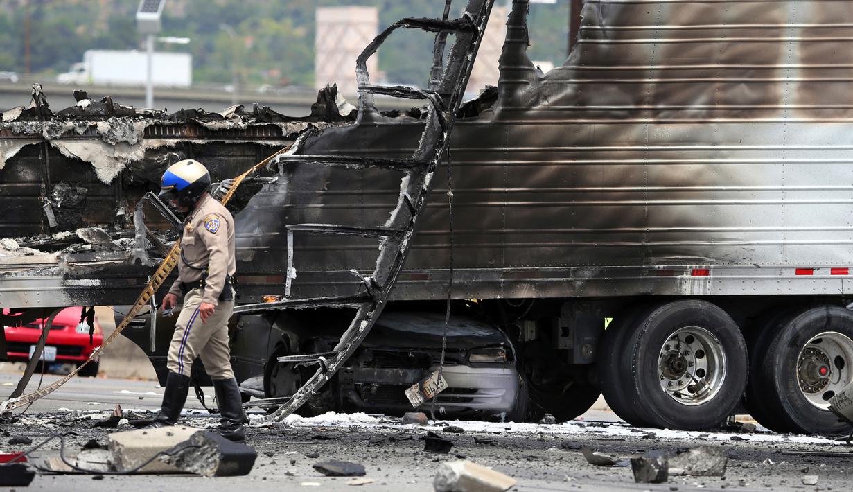 Petugas keamanan setempat memeriksa bangkai truk yang telah hangus usai terjadi tabrakan antara dua truk besar di utara pusat kota Los Angeles (25/4). (AP Photo/Reed Saxon)