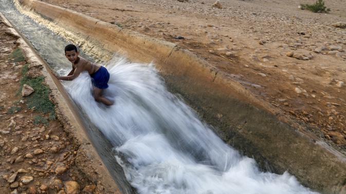 Seorang anak bermain di aliran mata air yang digunakan untuk irigasi untuk mendinginkan tubuh saat suhu udara mencapai 44 derajat Celcius di kota Jericho, Tepi Barat (1/9/2020). (AFP Photo/Ahmad Gharabli)