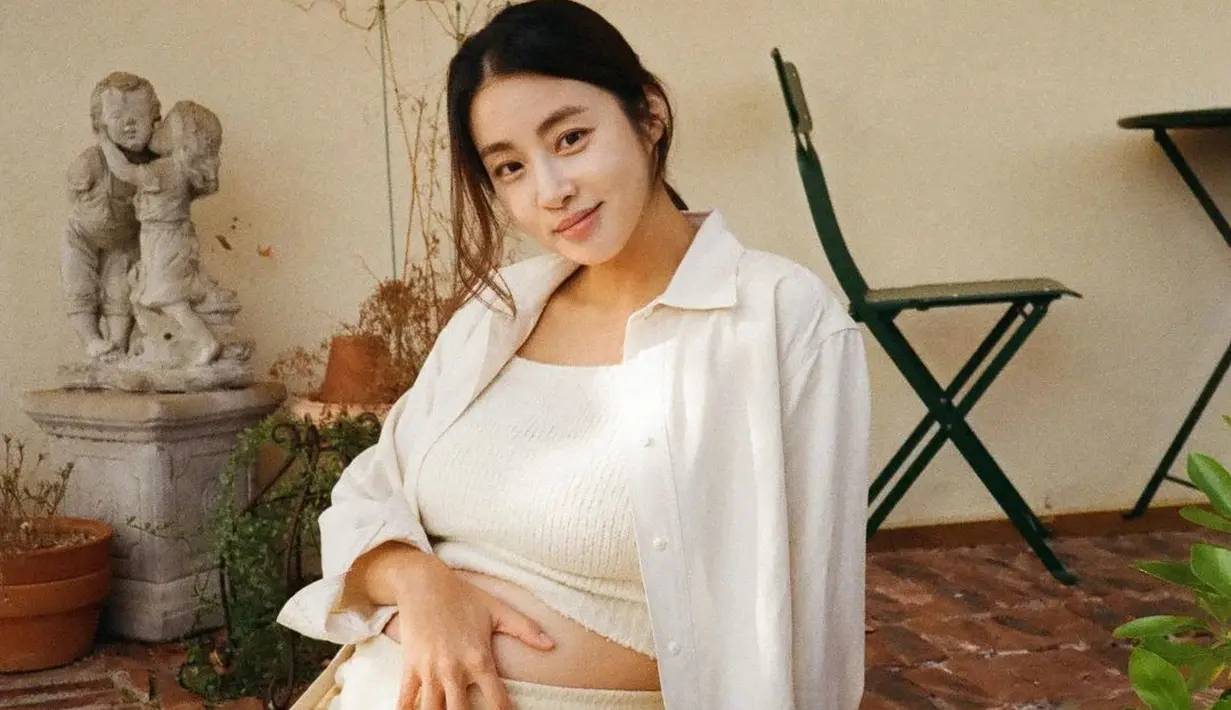 Saat foto sendiri, Kang Sora tampil bak bumil menggemaskan dengan outfit serba putih. Ia menggabungkan cropped knitwear dan celana training dengan kemeja oversized. [@reveramess_]