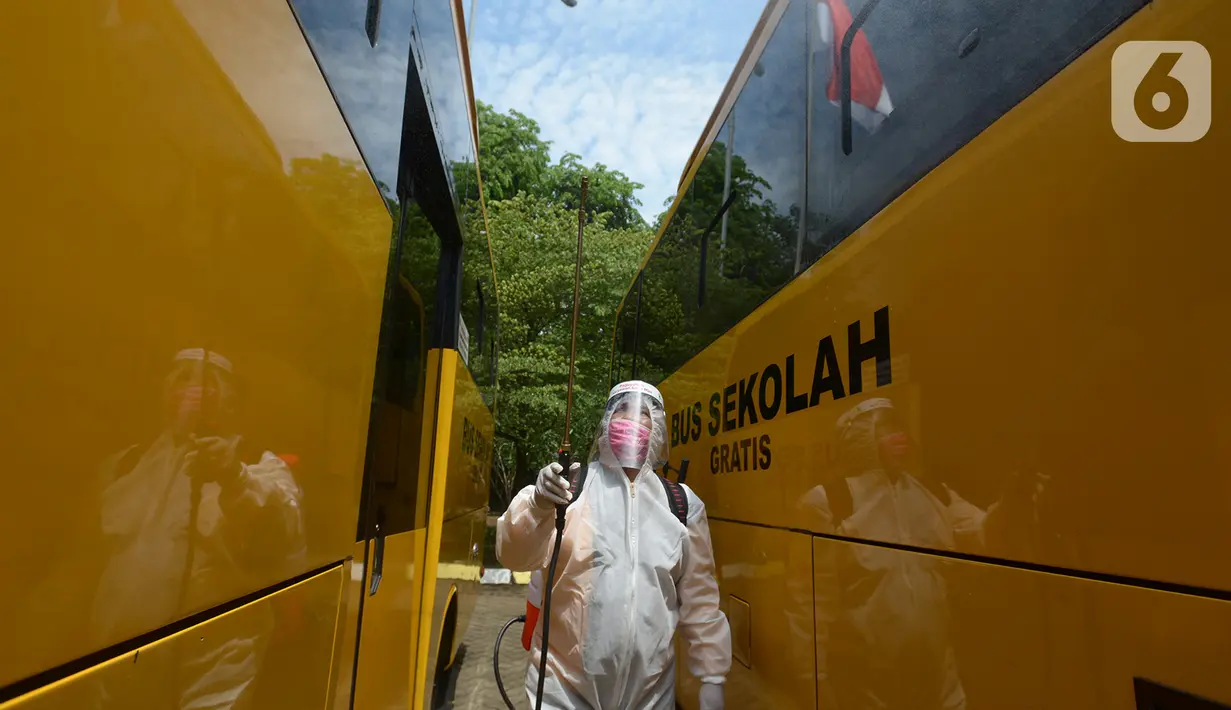 Petugas ber-APD menyemprotkan disinfektan pada bus sekolah di Posko Gabungan PSBB dan Gakplin Protkes, Puskesmas Jatinegara, Jakarta, (22/9/2020). Sejumlah unit bus sekolah kini dialihfungsikan menjadi kendaraan untuk mengantar pasien Covid-19 berstatus OTG menuju Wisma Atlet. (merdeka.com/Imam Buho